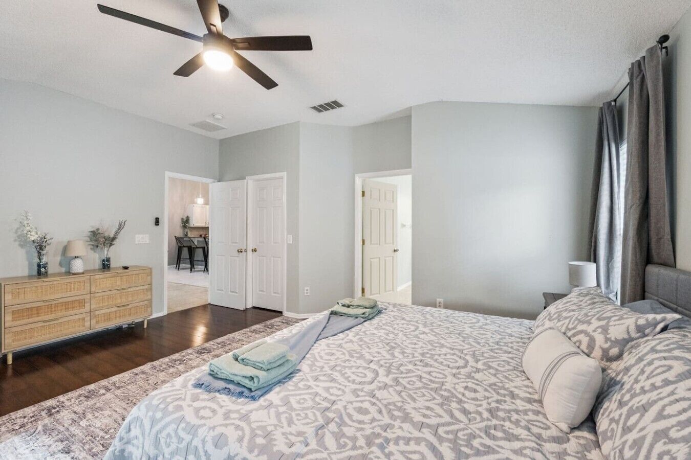 A bedroom with a bed, a dresser, a ceiling fan, and a door leading to another room.