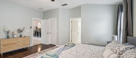 A bedroom with a bed, a dresser, a ceiling fan, and a door leading to another room.