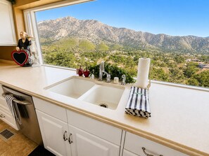 Una cucina con un lavello doppio, una finestra vista montagna e una statuetta decorativa sul bancone.