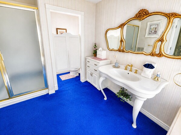 A bathroom with a white vanity, a gold-framed mirror, and a blue carpet.