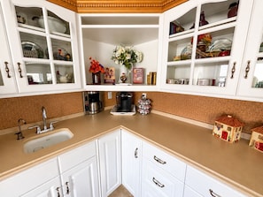 Una cucina con mobili bianchi, un lavandino, una macchina da caffè e oggetti decorativi.