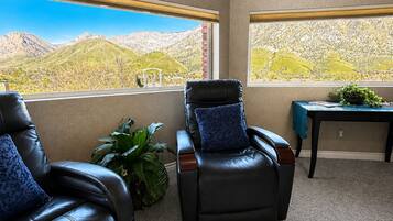 Una habitación con dos sillones de cuero, un reloj y vistas a las montañas a través de amplios ventanales.