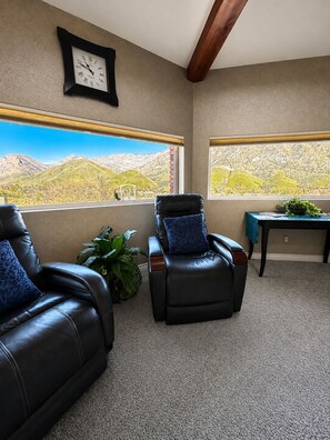 A room with two leather chairs, a clock, and a view of mountains through large windows.