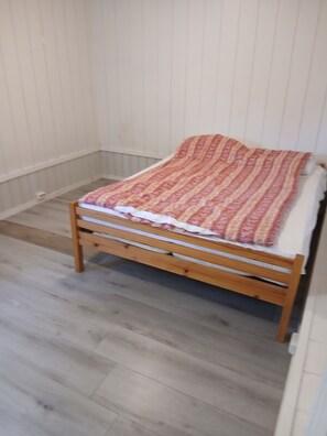 Un lit simple avec une couverture à motifs dans une pièce dont le sol est en bois et les murs sont blancs.