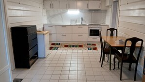 Cocina compacta con armarios blancos, refrigerador, lavamanos y una zona de comedor con sillas.