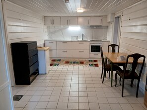 Une cuisine compacte avec des meubles blancs, un réfrigérateur, un évier et un coin repas avec des chaises.