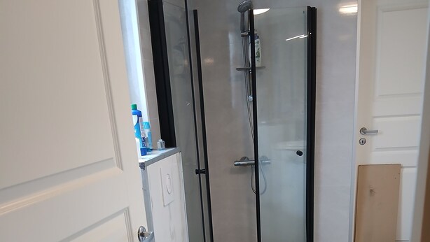 Un baño moderno con inodoro, cabina de ducha con mampara de vidrio y suelo con azulejos blancos.