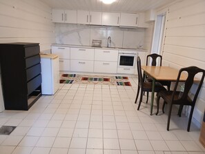 Une cuisine de taille réduite avec des meubles blancs, une table à manger en bois et un tapis à motifs.