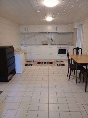 A kitchen with white cabinets, a tiled floor, a dining table with chairs, and a small rug.