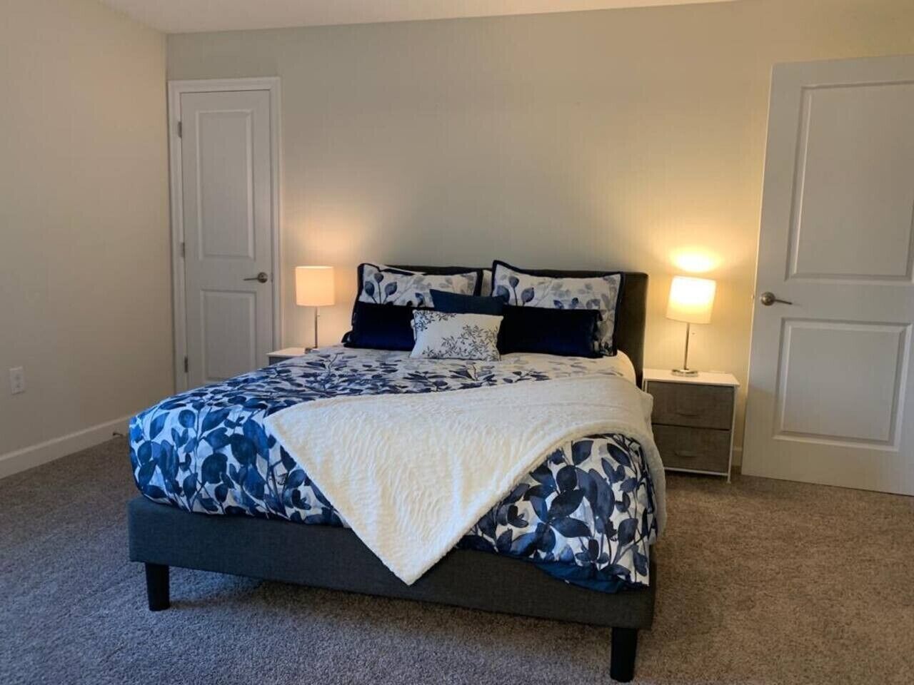 A bedroom with a bed, two bedside tables, and two doors.