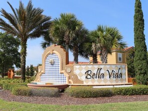 Ein Schild mit der Aufschrift 'Bella Vida', umgeben von Palmen und einem Brunnen.