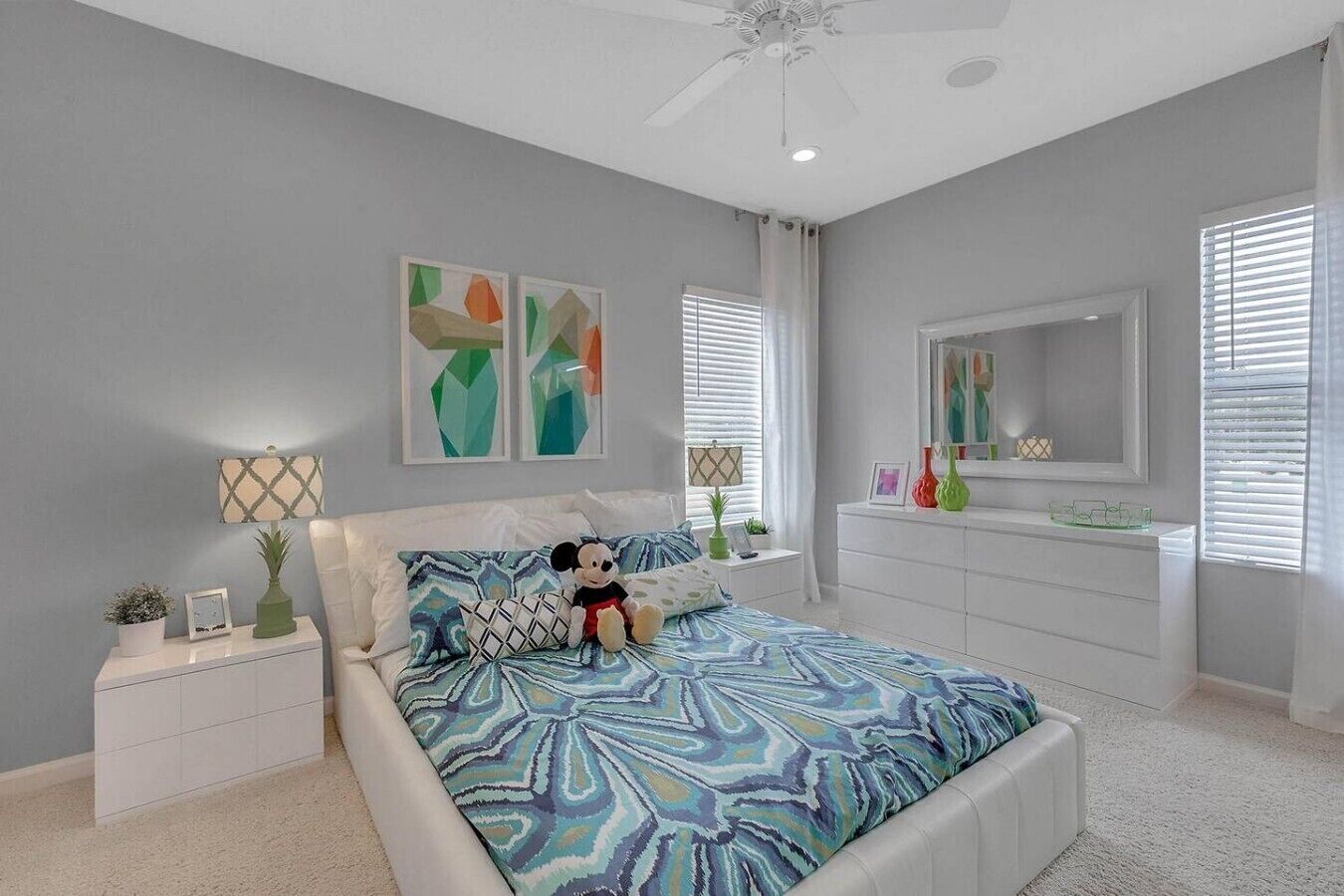 A bedroom with a bed, nightstands, a dresser, a ceiling fan, and artwork on the walls.