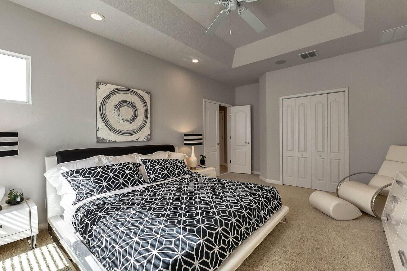 A bedroom with a bed, a nightstand, a lamp, a ceiling fan, and a door.