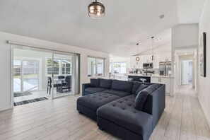 A modern living room with a sectional sofa, a dining area with a table and chairs, and a kitchen with white cabinets and appliances. - Luxury Coastal Haven, Pool, Beach, Golf and Relax (Palm Coast)