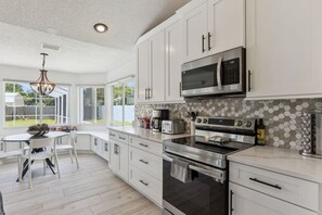 A modern kitchen with white cabinetry, a built-in microwave, a double oven, and a dining area with a round table and chairs. - Luxury Coastal Haven, Pool, Beach, Golf and Relax (Palm Coast)