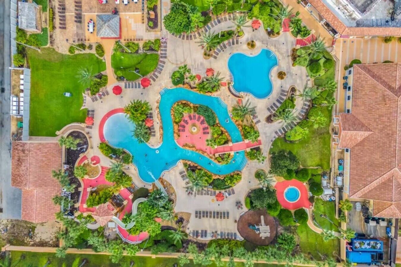 Vue aérienne d’un complexe hôtelier doté de plusieurs piscines, de jardins aménagés et d’une fontaine centrale.