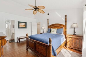 Ein Schlafzimmer mit einem hölzernen Bett, einem Deckenventilator, Nachttischlampen und einer Tür zu einem anderen Raum.