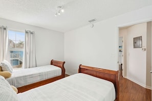 Ein Hotelzimmer mit zwei Einzelbetten, einem fensterbelaubten Fenster, einem Blick auf einen Balkon und einer Tür zu einem weiteren Raum.