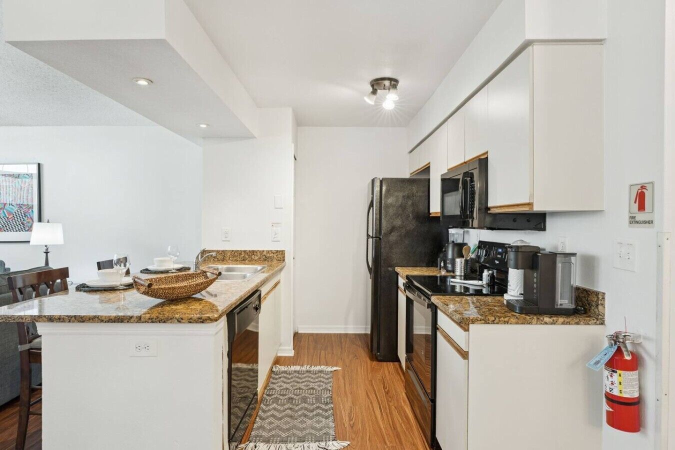 A modern kitchen with white cabinetry, granite countertops, a refrigerator, microwave, and coffee maker.