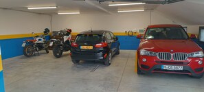 Eine Parkgarage mit drei Fahrzeugen: einem Motorrad, einem schwarzen SUV und einem roten BMW.