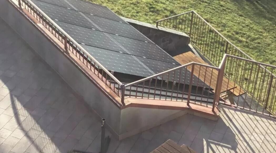 Une terrasse sur le toit équipée de panneaux solaires, d’une plateforme en bois et d’une rambarde en métal.