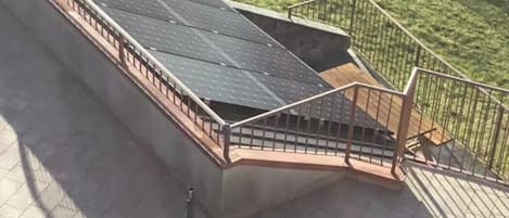 A rooftop with solar panels, a wooden deck, and a metal railing.