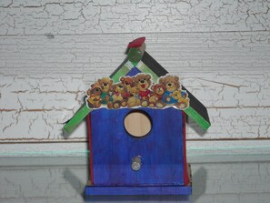 Een houten vogelhuisje met een blauwe basis en een groen dak, versierd met plakkers van teddyberen.