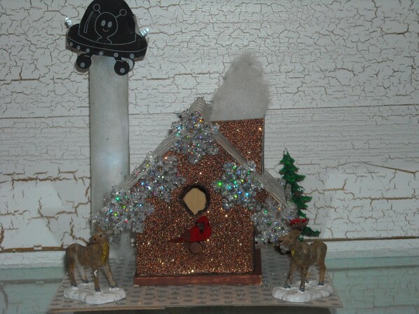 Een miniatuur kersttafereel met een huis, rendieren en een sneeuwpop.