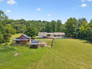 Une propriété rurale comprenant une grange, une grande maison et une piscine entourée d’une clôture.
