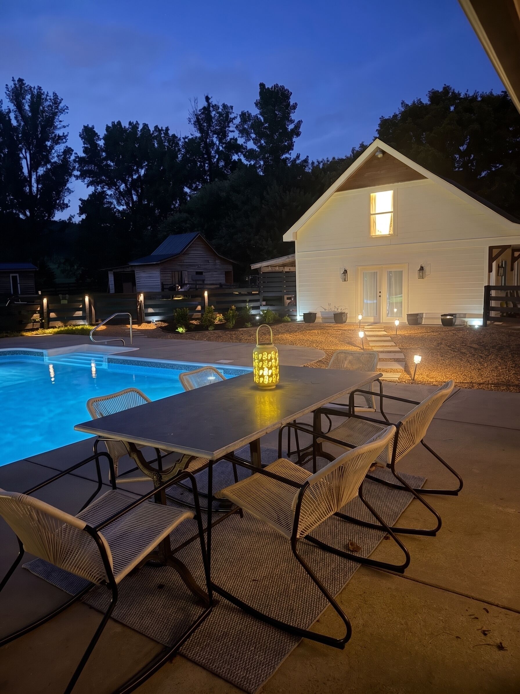 Un espace aménagé au bord de la piscine avec une table et des chaises, une petite maison en arrière-plan et un ciel dégagé.