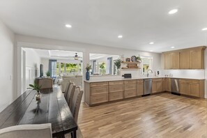 A modern kitchen with wooden cabinets, a central island, and a dining area with a dark wooden table and chairs.