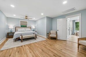 Une chambre à coucher comprenant un lit, des tables de chevet, une chaise, un ventilateur de plafond et une porte donnant sur un espace extérieur.