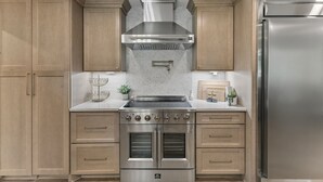 A kitchen with wooden cabinets, a stainless steel range hood, double ovens, and a refrigerator.