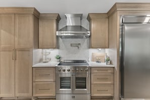 A kitchen with wooden cabinets, a stainless steel range hood, double ovens, and a refrigerator. - Your Franklin Oasis (Franklin)