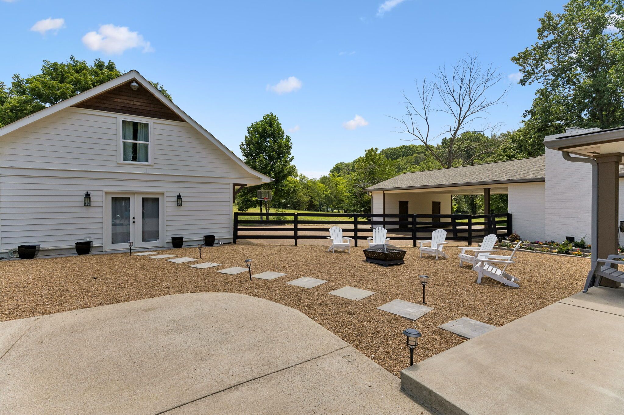 A property with a white building, outdoor seating area with Adirondack chairs, and a fenced yard.