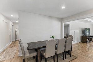 A dining area with a wooden table and chairs, a small plant, and a view into another room.