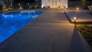 A swimming pool with a metal ladder, a basketball hoop, and a house with a porch.