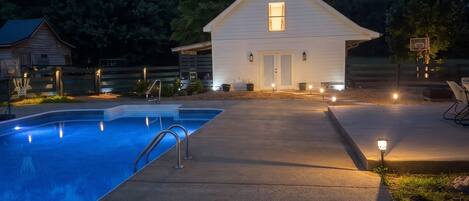 A swimming pool with a metal ladder, a basketball hoop, and a house with a porch.