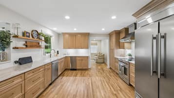 A modern kitchen with wooden cabinets, stainless steel appliances, and a herringbone wood floor.