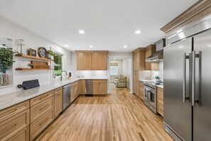 A modern kitchen with wooden cabinets, stainless steel appliances, and a herringbone wood floor.