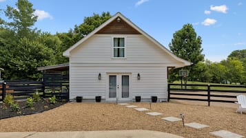 A two-story white house with a front porch, a wooden fence, and a basketball hoop.