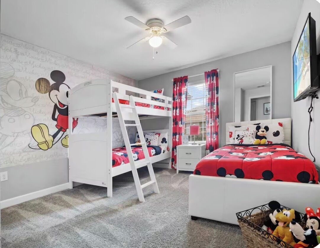 A child's bedroom with a bunk bed, Mickey Mouse wall art, a ceiling fan, and a television.