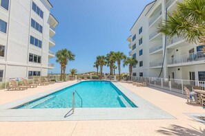 A swimming pool surrounded by lounge chairs and palm trees, with a clear sky above. - Read  the Reviews!Right on the Beach with East and West Views! Cannot get any closer to the Water! (Orange Beach)