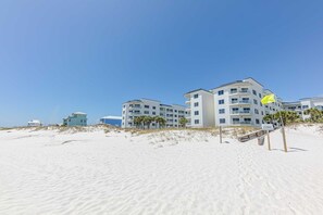 Et hotel ved stranden med flere etager, en sandstrand i forgrunden og en klar blå himmel.