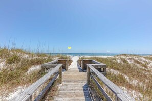 Une promenade en bois qui mène à une plage bordée de dunes de sable, sous un ciel bleu et dégagé.