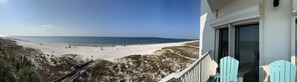 Une vue sur la plage depuis un balcon, avec un ciel dégagé, une plage de sable et une clôture en bois.