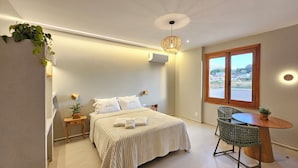 A bedroom with a bed, bedside tables, a small round table with a chair, a window with a view, and a hanging plant. - Casa Aurora – Parque da Estalagem Condominium (Pirenópolis)