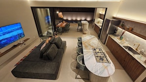 Una sala moderna con sofá, comedor con sillas, cocina con encimera de mármol y televisor montado en la pared.