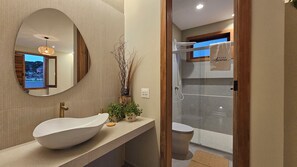 A modern bathroom with a large oval sink, a mirror, and a glass-enclosed shower. - Vrbo Property (Pirenópolis)