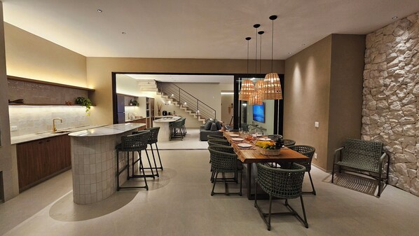 A modern kitchen with a bar area, a dining space with wicker chairs, and a stone accent wall. - Vrbo Property (Pirenópolis)